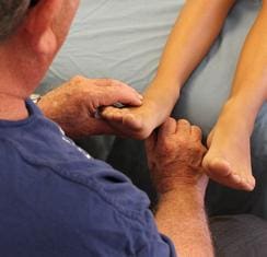 A person examines the foot and ankle of another individual who is lying on a surface.